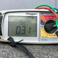 A Megger MFT1721 tester displays a reading of 0.31 ohms and 7.35 amps. Colored test leads are connected, and the device is placed on a concrete surface outdoors.