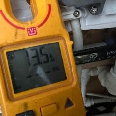 A yellow digital clamp meter displays a reading of 1.35 A AC, measuring current from a brown electrical wire near a junction box with multiple cables and connectors.